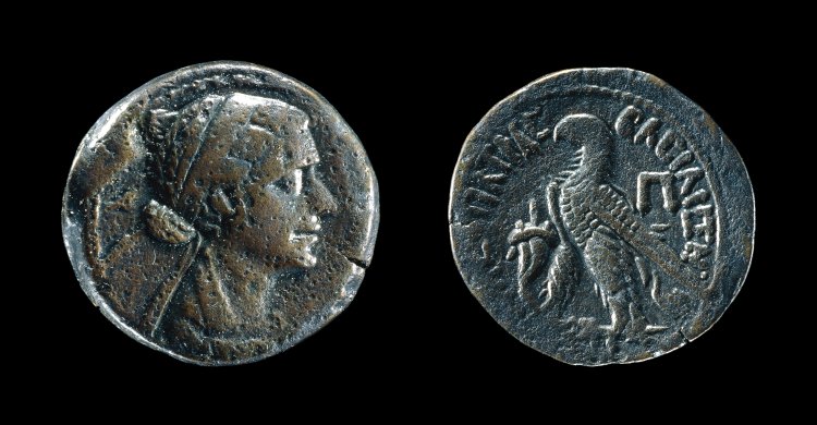 Double-sided copper alloy coin. On the left, one side of the coin depicts a Macedonian Cleopatra VII with her hair in a low smooth bun and a diadem, her head facing the right. On the right, the other side of the coin depicts a standing eagle facing the left.