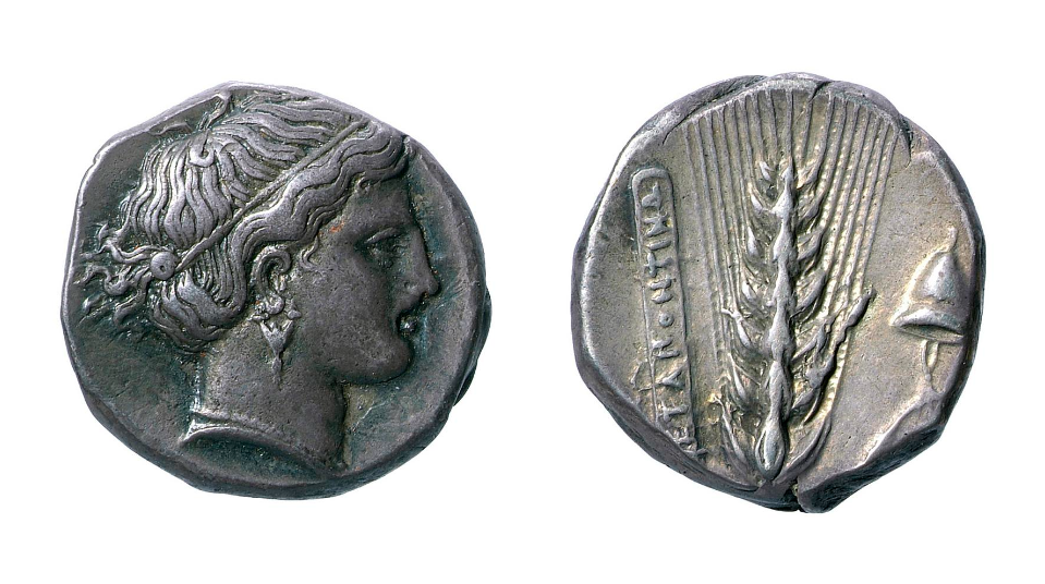 Double-sided coin of the Greek Goddess Demeter. On the left, one side of the coin displays the head of Demeter facing the right with her hair tied back with a band. On the right, the other side of the coin displays an ear of barley and a helmet.