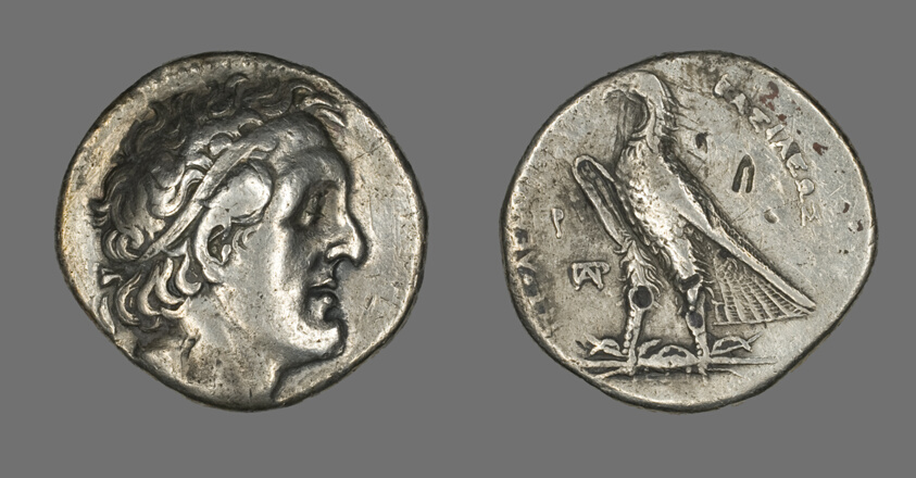 Double-sided silver coin of Ptolemy I Soter. On the left, one side of the coin displays the head of Ptolemy I facing the right. On the right, the other side of the coin depicts an eagle standing on a thunderbolt and facing the left.